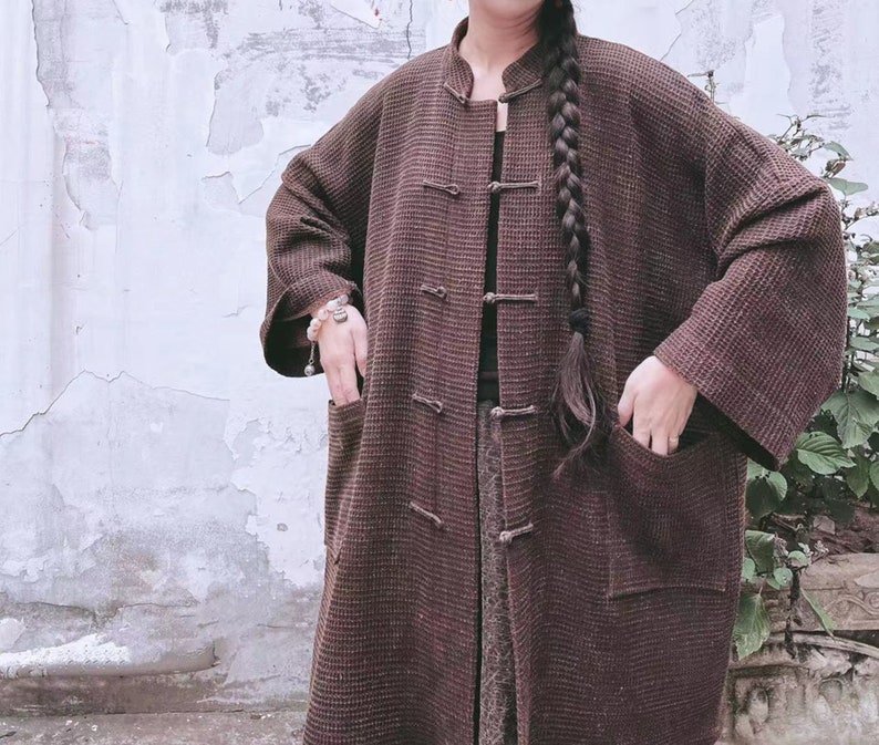 May include: A long brown waffle-textured coat with a mandarin collar and multiple buttons down the front. The coat has two large pockets on the sides.