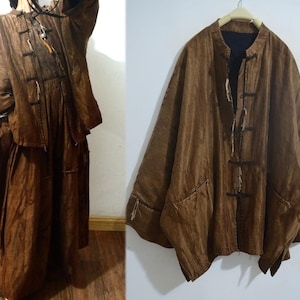 Puede incluir: Conjunto de chaqueta y falda de lino marrón. La chaqueta tiene cuello mandarín, cierres de rana y dos bolsillos delanteros. La falda es larga y fluida. El conjunto está hecho de una tela texturizada y tejida.