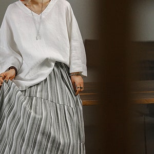 May include: A white linen top with a v-neck and long sleeves paired with a grey and white striped skirt.
