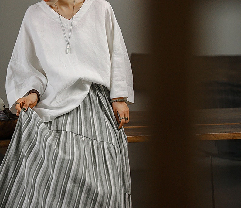 May include: A white linen top with a v-neck and long sleeves paired with a grey and white striped skirt.