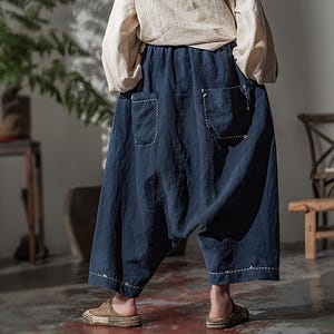 May include: Navy blue cropped pants with two front pockets and white stitching details. The pants have a relaxed fit and an elastic waistband. The model is wearing a cream-colored long-sleeve shirt and brown sandals.