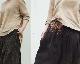 May include: A beige long-sleeved sweater and dark brown, wide-legged trousers. The trousers have a decorative floral design on the side. The outfit is casual and comfortable, suitable for everyday wear.