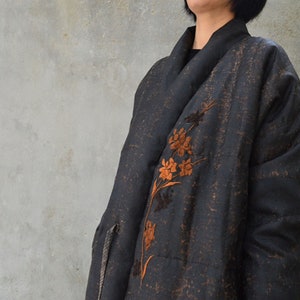 Könnte beinhalten: Eine schwarze Jacke mit langen Ärmeln und einem floralen Stickmuster in Braun und Orange. Die Jacke hat einen Schalkragen und eine lockere Passform.