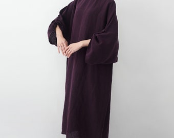 Puede incluir: Un vestido largo de color púrpura oscuro con cuello redondo y mangas anchas y abullonadas. El vestido tiene una silueta suelta y fluida, y parece estar hecho de una tela suave y natural. Las mangas están recogidas en el codo, lo que añade al diseño único del vestido.