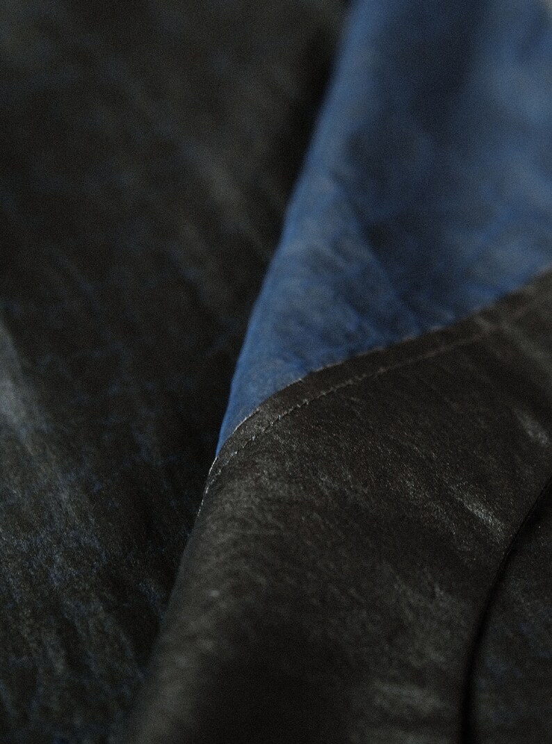 Puede incluir: Primer plano de una tela azul oscuro con una tela negra doblada sobre ella. La tela tiene una textura casi de mezclilla.