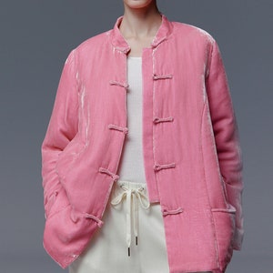 May include: A pink velvet jacket with a mandarin collar and frog closures. The jacket has long sleeves and two front pockets. The model is wearing a white top and white trousers.