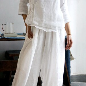 May include: A white linen wrap top with a long tie and matching wide-leg pants. The top has a V-neck and three-quarter sleeves.