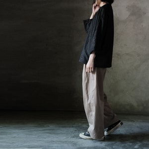 Puede incluir: Una persona con una camisa negra de manga larga y pantalones beige. Lleva zapatillas negras con suela blanca.