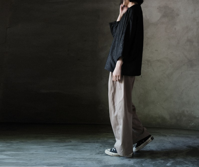 Puede incluir: Una persona con una camisa negra de manga larga y pantalones beige. Lleva zapatillas negras con suela blanca.