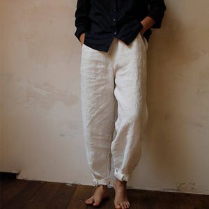 May include: White linen trousers with a relaxed fit and cuffed hems. The trousers are made from a lightweight fabric and have a casual style.