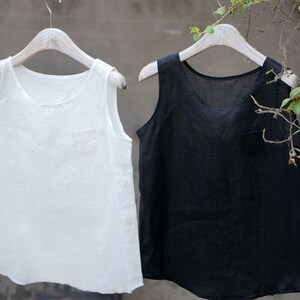 May include: Two sleeveless shirts hanging on hangers. The shirt on the left is white and the shirt on the right is black.