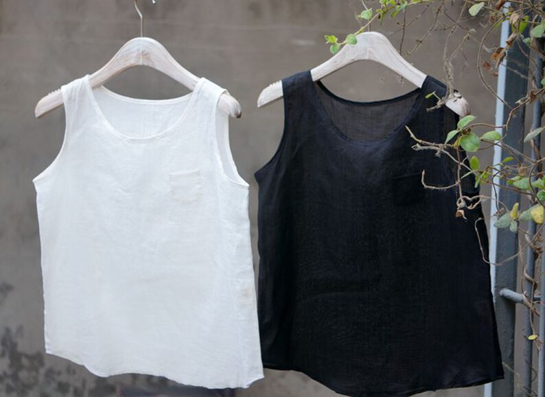 May include: Two sleeveless shirts hanging on hangers. The shirt on the left is white and the shirt on the right is black.