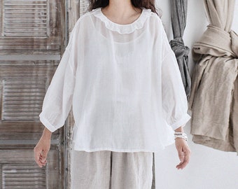 May include: A white, lightweight, loose-fitting blouse with a ruffled neckline and long sleeves. The blouse is made of a sheer fabric and has a relaxed fit.