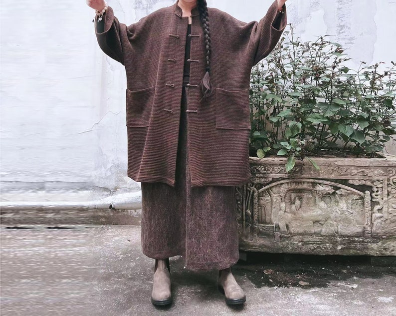 May include: A brown long-sleeved jacket with a mandarin collar and a matching brown skirt. The jacket has a button closure and pockets. The skirt is knee-length and has a straight silhouette.