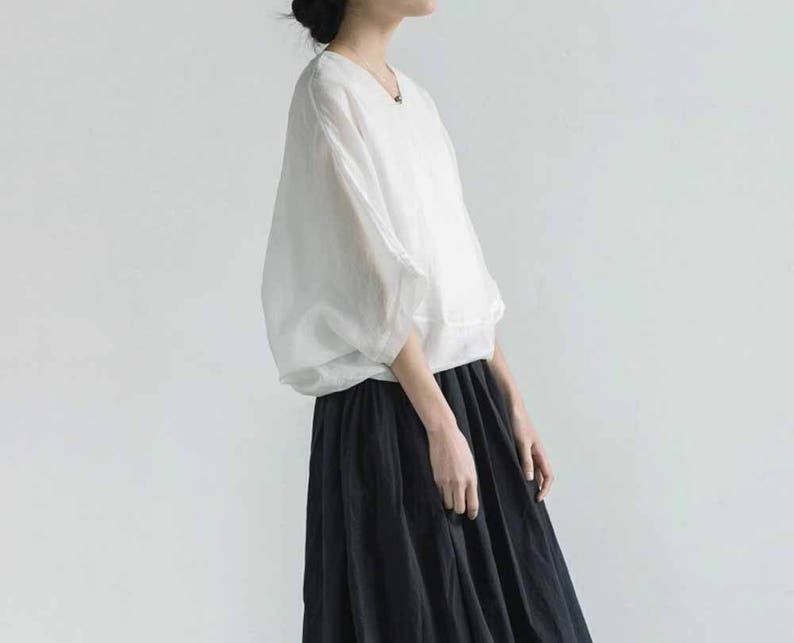 May include: A white, loose-fitting blouse with a v-neckline and long sleeves. The blouse is paired with a black, flowy skirt.