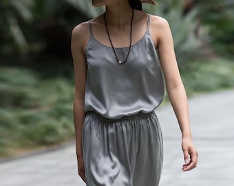 May include: A light grey silk camisole top with thin straps and a matching high-waisted, elastic-waist pants. A black necklace with a single pearl hangs around the neck. The outfit is worn outdoors.