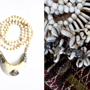 May include: A long necklace made of white beads with a large, crescent-shaped pendant. The pendant is made of bone and has silver accents. The necklace is displayed on a white background.
