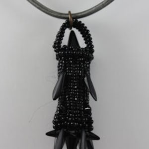 Könnte beinhalten: Eine schwarze Perlenkette mit einem Anhänger in Form eines stilisierten Turms mit einer spitzen Spitze. Der Anhänger besteht aus kleinen schwarzen Perlen und hat eine Reihe von spitzen Stacheln am Boden.