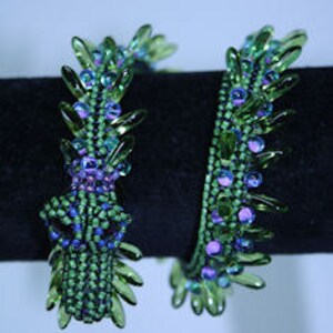 Op de afbeelding: Twee groene kralenarmbanden met paarse en blauwe accenten. De armbanden zijn gemaakt van kleine, gefacetteerde kralen en hebben een stekelig, getextureerd ontwerp.
