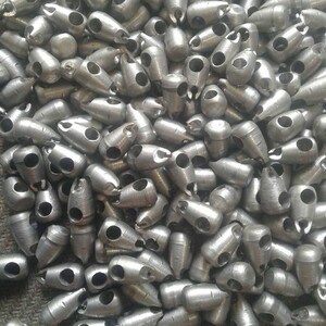 May include: A pile of silver metal beads with two holes each. The beads are shaped like a teardrop with a pointed end.