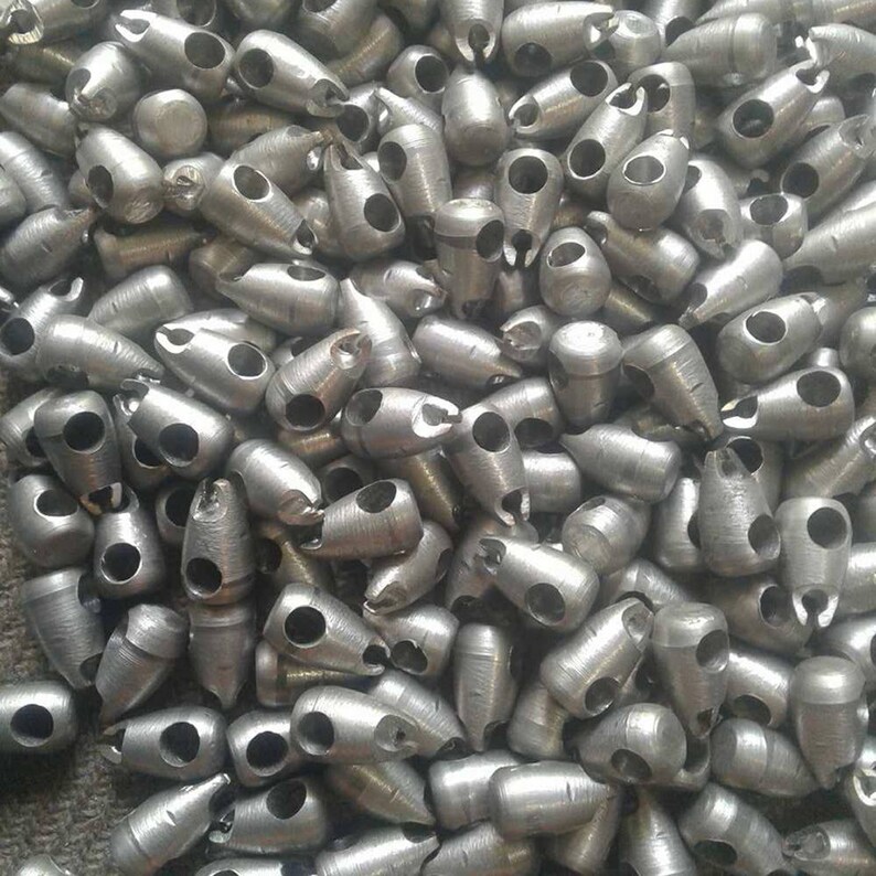 May include: A pile of silver metal beads with two holes each. The beads are shaped like a teardrop with a pointed end.
