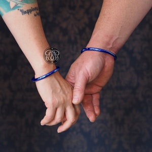 May include: Two people holding hands, each wearing a blue glass bangle bracelet.