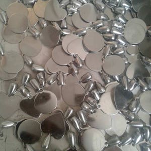 May include: A close-up of a pile of silver metal charms. The charms are in the shape of circles and hearts. The charms have a shiny finish.