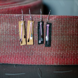 May include: Four pairs of dangle earrings with silver chain and leather accents. Two pairs have brown leather accents and two pairs have black leather accents.