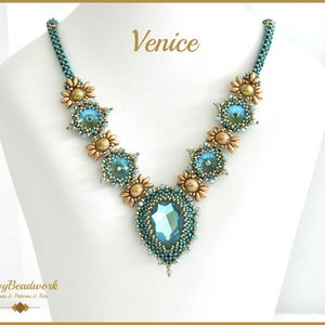 Op de afbeelding: Een turquoise kralenketting met een grote, druppelvormige hanger. De ketting heeft goudkleurige accenten en blauwgroene edelstenen. Het woord "Venice" is in gouden letters geschreven. De ketting wordt gepresenteerd op een witte mannequin.