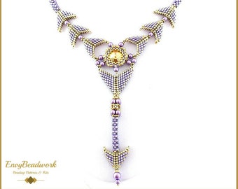 May include: A beaded necklace with a purple and gold color scheme. The necklace features a large, clear crystal in the center and a pendant that hangs down from the center. The necklace is called "Yvonne".