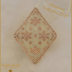 Op de afbeelding: Een witte en koperen kerstversiering in de vorm van een diamant. De versiering heeft een geometrisch patroon en hangt aan een wit touwtje.