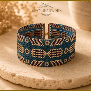 Op de afbeelding: Een brede armband gemaakt van teal, donkerpaarse en gouden kraaltjes in een geometrisch patroon. De armband is voorzien van een goudkleurige metalen sluiting en bevat de tekst ENVYBEADWORK en 2026-A004 op de afbeelding.