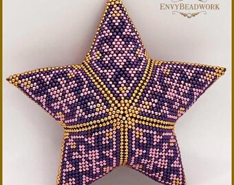 May include: A five-pointed star ornament crafted from small beads in shades of purple, light pink, and metallic gold. The surface features a geometric pattern with gold bead lines separating the sections. Text reads ENVYBEADWORK and 2026-005.