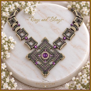 Op de afbeelding: Een kralenketting met een grote centrale ruitvormige hanger met een paars kristal in het midden, omringd door kleinere vierkante kralenschakels in metallic goud, groen en paars. De tekst Rings and Blings en ENVYBEADWORK zijn zichtbaar.