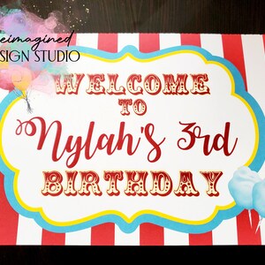 Peut inclure: Une pancarte blanche avec des rayures rouges et bleues autour du bord. La pancarte dit "Bienvenue &agrave; Nylah's 3rd Birthday" en lettres rouges et dor&eacute;es. Il y a des ballons color&eacute;s et de la barbe &agrave; papa sur la pancarte.