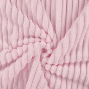 Può includere: Primo piano di un tessuto morbido, rosa, a coste. Il materiale è disposto in un motivo a spirale, con creste verticali che creano una superficie strutturata. La consistenza morbida e il colore rosa chiaro suggeriscono un tessuto accogliente e confortevole, adatto a coperte o abbigliamento.