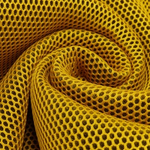 Könnte beinhalten: Nahaufnahme eines gelben Netzstoffes mit einem Wabenmuster. Der Stoff ist gefaltet und verdreht, wodurch ein wirbelnder Effekt entsteht.