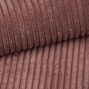 Könnte beinhalten: Nahaufnahme eines Abschnitts eines Cordstoffes in einem gedämpften Rosaton. Der Stoff hat eine gerippte Textur mit vertikalen Linien, die ein weiches, plüschiges Aussehen erzeugt. Die Falten und Schatten verleihen dem Material Tiefe.