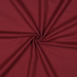Könnte beinhalten: Nahaufnahme eines tief burgunderfarbenen Stoffes mit einem Wirbelmuster. Der Stoff ist dicht gewebt, mit sichtbarer Textur und Falten, die vom Zentrum ausgehen. Die Farbe ist ein satter, einfarbiger Farbton, der auf ein hochwertiges Textil hindeutet.