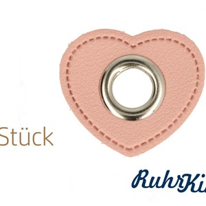 May include: Two pink leather heart-shaped tags with a silver metal eyelet in the centre. The text "2 Stück" is visible below the tags.