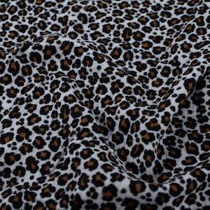 Könnte beinhalten: Ein Stoffstück mit einem sich wiederholenden Leopardenmuster. Das Design besteht aus schwarzen und braunen Flecken auf weißem Hintergrund. Das Material ist in weichen Falten und Knicken dargestellt, was eine strukturierte Optik erzeugt.