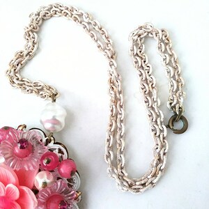 May include: A pink and white flower cluster pendant necklace with a faux pearl drop and a white chain.