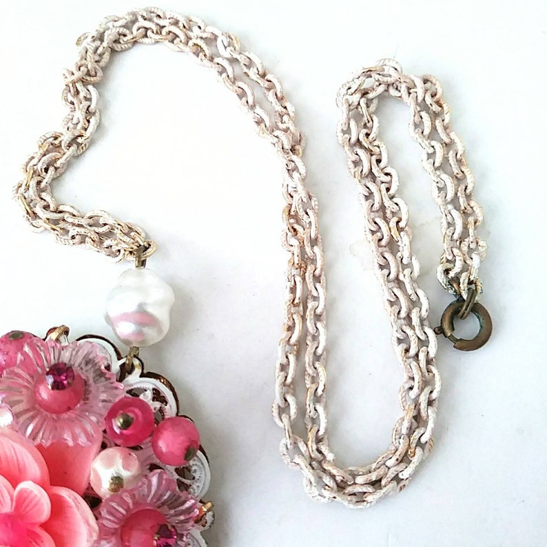 May include: A pink and white flower cluster pendant necklace with a faux pearl drop and a white chain.
