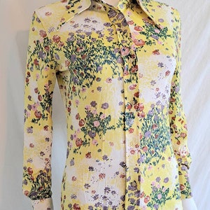 May include: A yellow long-sleeved button-up shirt with a floral print. The shirt has a wide collar and a fitted silhouette.