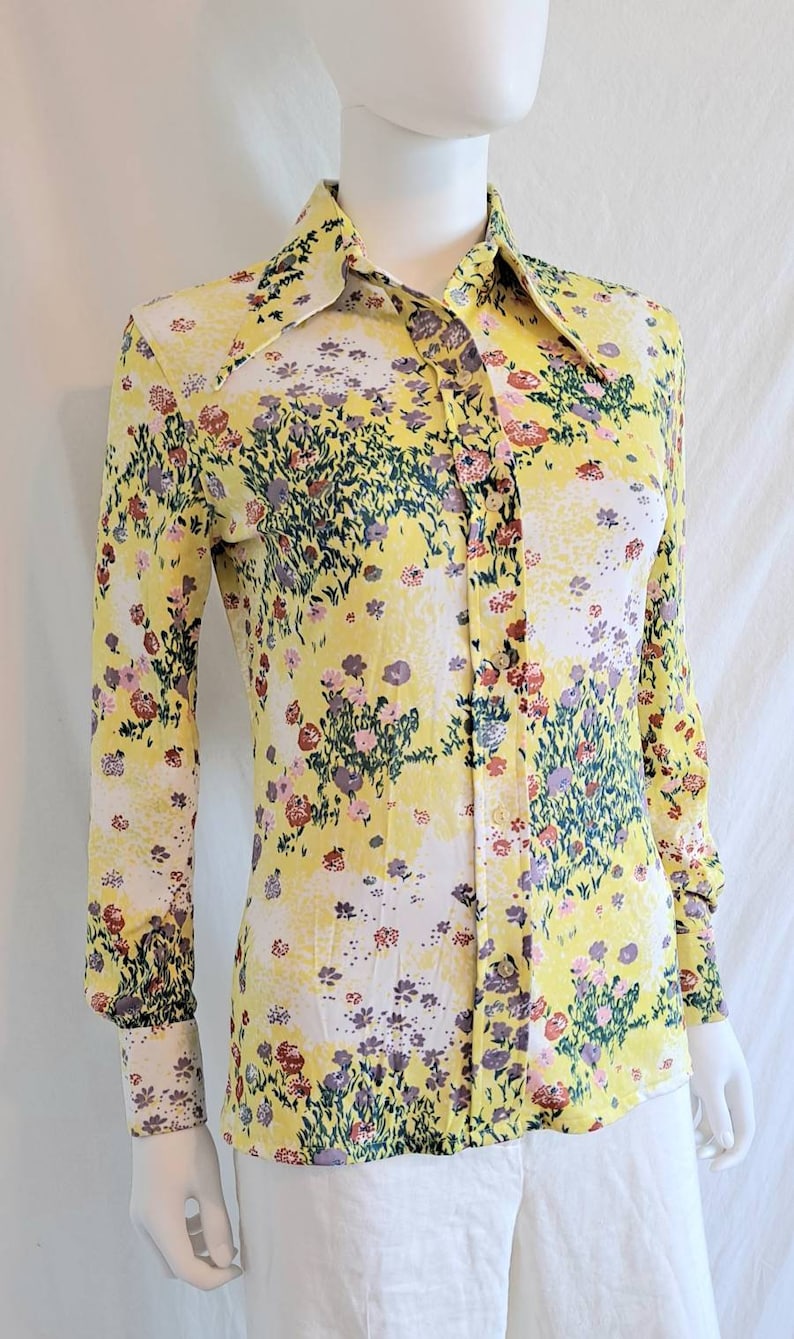 May include: A yellow long-sleeved button-up shirt with a floral print. The shirt has a wide collar and a fitted silhouette.