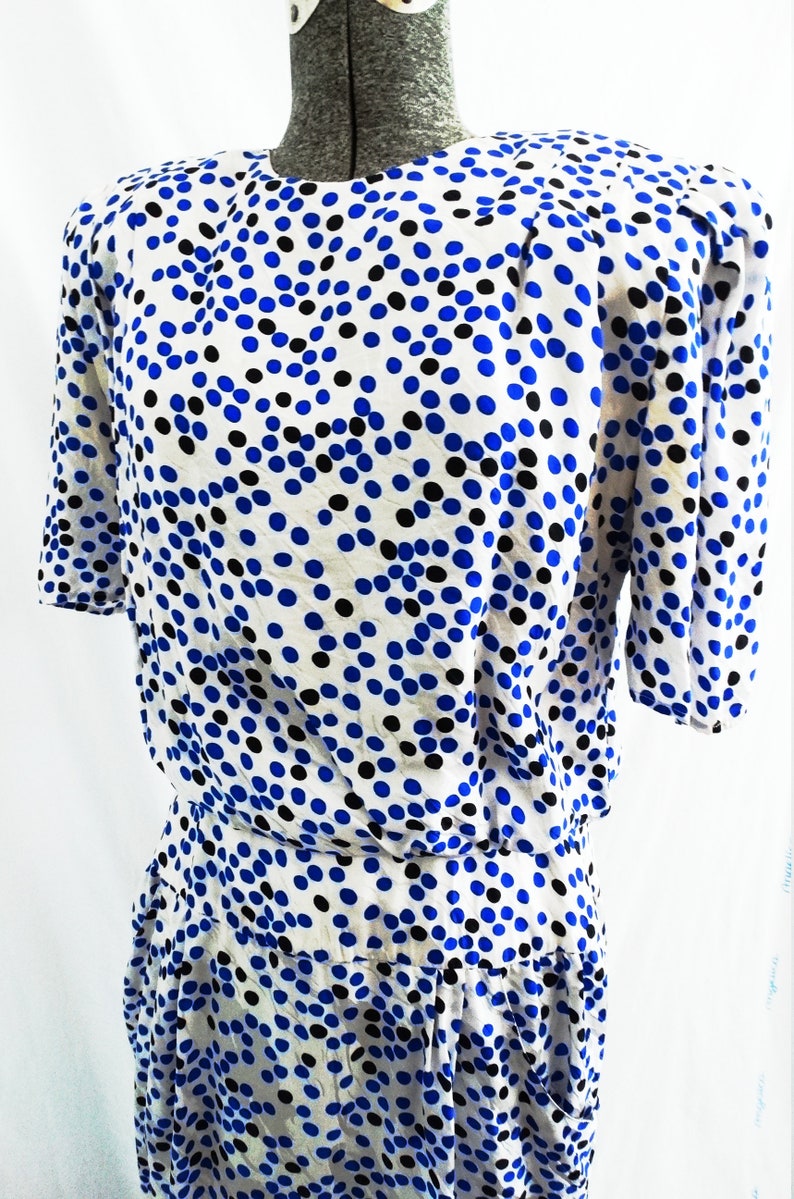May include: A white dress with a blue and black polka dot pattern. The dress has a short sleeve and a fitted bodice. The skirt is gathered at the waist.