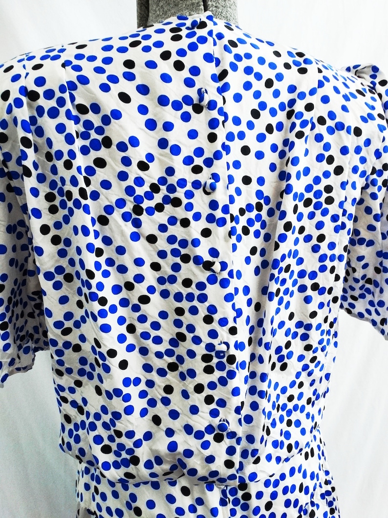 May include: A white dress with a blue and black polka dot pattern. The dress has a button closure down the back.
