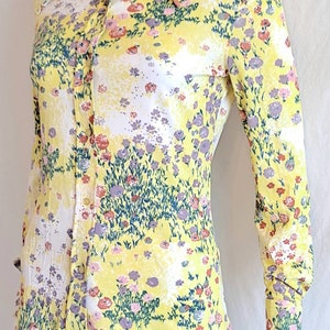May include: A yellow long-sleeved shirt with a floral print. The shirt has a pointed collar and button closure.