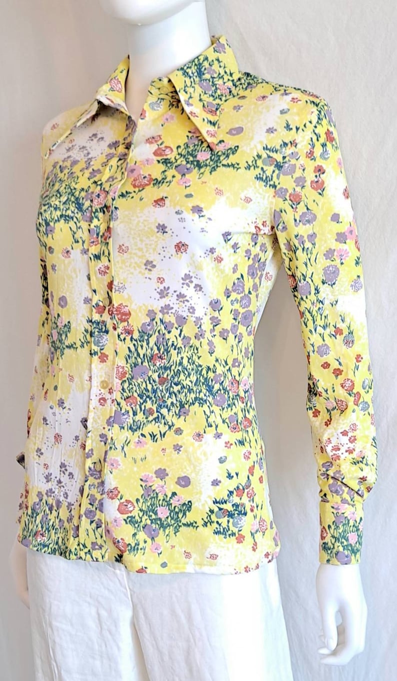 May include: A yellow long-sleeved shirt with a floral print. The shirt has a pointed collar and button closure.