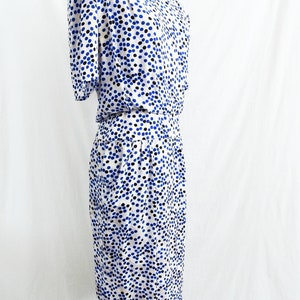 May include: A white dress with a blue and black polka dot pattern. The dress has short sleeves and a fitted bodice. The skirt is slightly flared and falls to the knees.